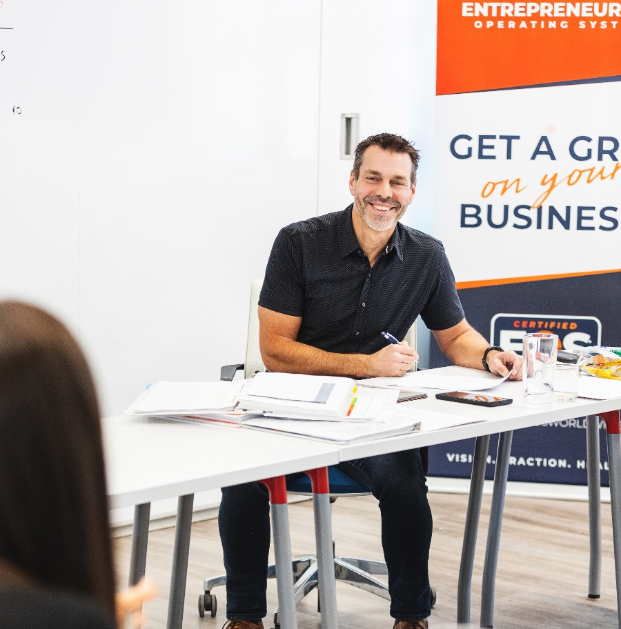 Jon Weening smiling while sitting at a table near EOS signage