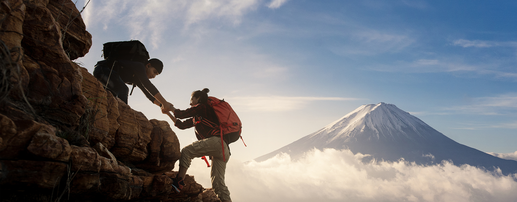 A mountain climber helping another mountain climber climb up over a ledge