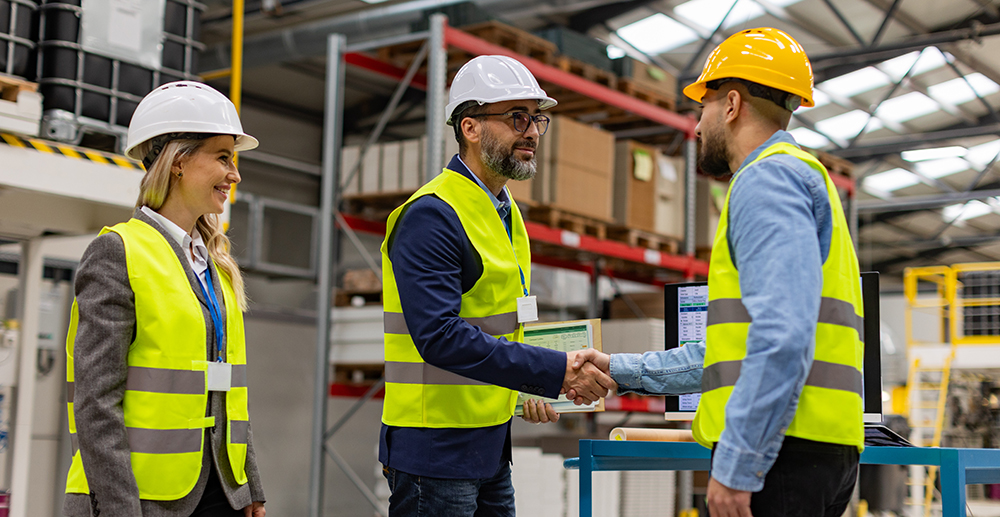 A business leader wearing a hardhat shaking hands with a construction employee
